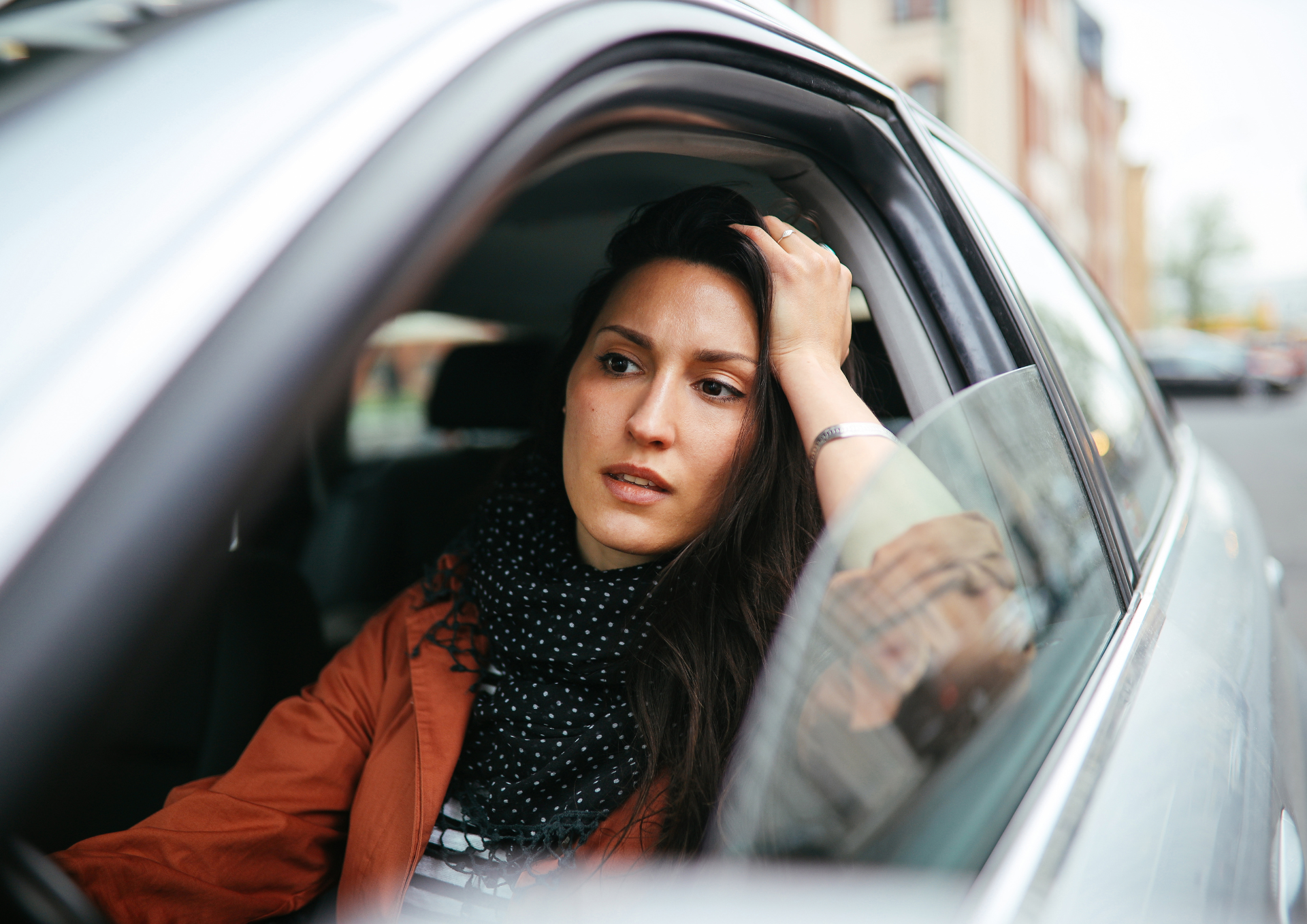 Woman sitting in traffic looking stressed, symbolizing how limiting beliefs can show up in everyday moments.